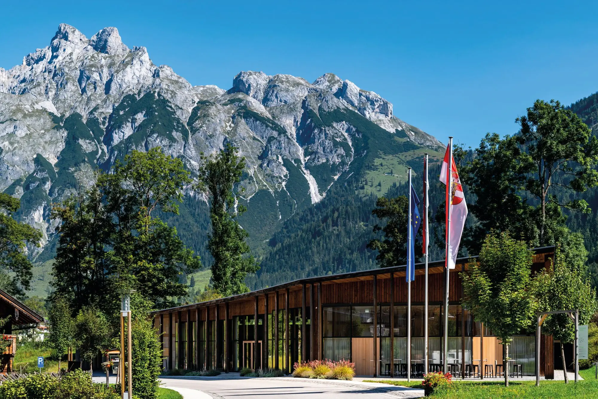 Tagungszentrum mit Flaggen vor Bergkulisse.