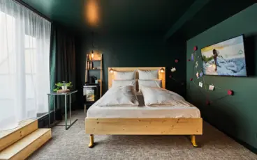 Modernes Hotelzimmer im Urban Nature mit einem minimalistischen Holzbett, dunkelgrünen Wänden, gemütlicher Beleuchtung, einem Wanddisplay, kreativem Wanddesign, einem kleinen Tisch mit Pflanze und einer großen Fensterfront mit fließenden Vorhängen.