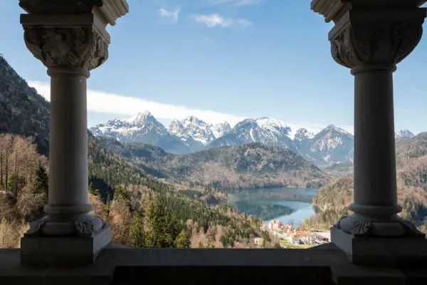 Ausblick Schloss Neuschwanstein Blick auf einen See und Berge durch zwei Säulen.