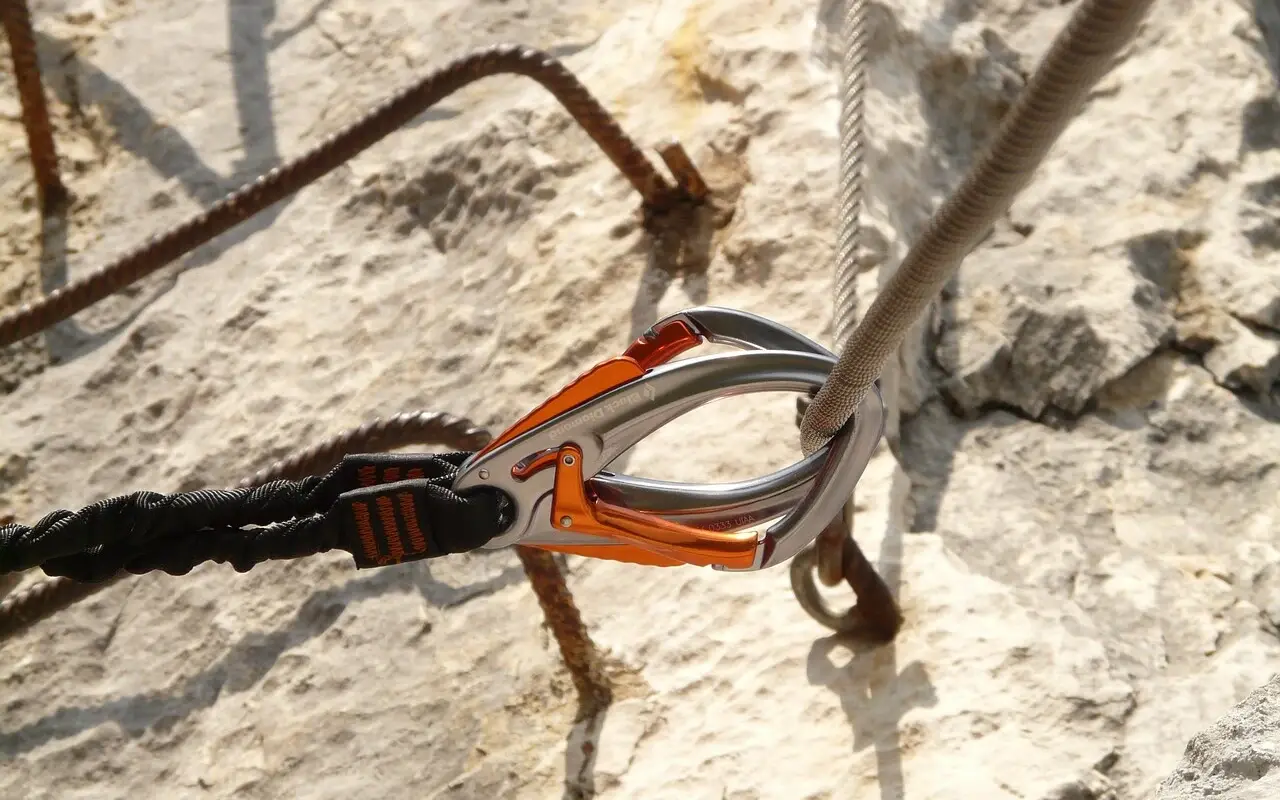 Klettern Österreich Nahaufnahme eines Karabiners, der an einem Drahseil in einem Felsen festgemacht ist.