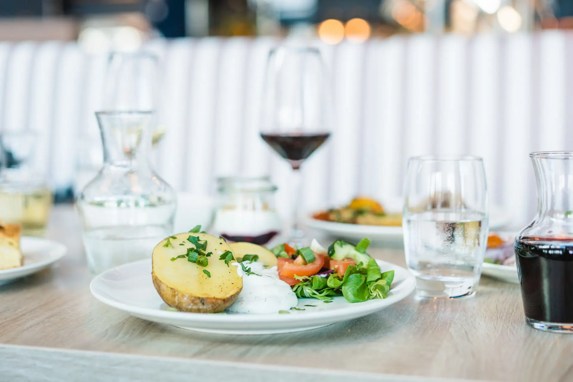 Ein gedeckter Esstisch mit einer vegetarischen Speise aus einer großem Kartoffel und Gemüse. Daneben stehen Wein- und Wassergläser.